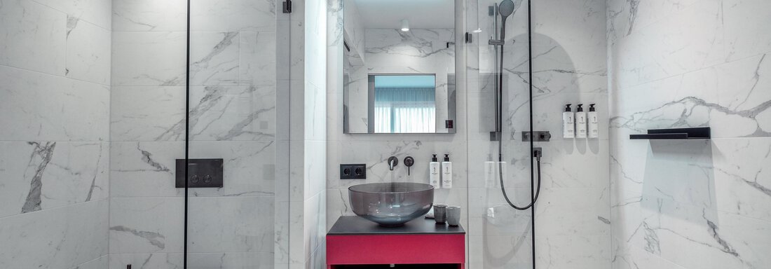 A modern bathroom with marbled walls and a glass shower. There is an elegant sink and a striking red shelf. - AlpenParks The Secret Sölden - Sölden