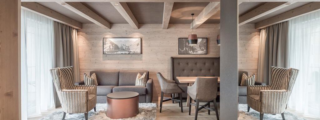 SMALL SECRET A modern living room with wooden ceilings and large windows. Cozy armchairs and a dining table create an inviting atmosphere. - AlpenParks The Secret Sölden - Sölden