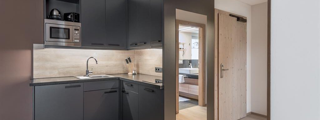 A modern kitchen with dark cabinets and a bright countertop. The room is well-lit and has access to another living area. - AlpenParks The Secret Sölden - Sölden