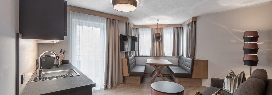 A modern living room with a cozy seating area and a small kitchenette. Large windows provide plenty of daylight. - AlpenParks The Secret Sölden - Sölden