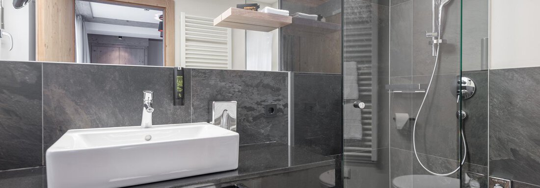 A modern bathroom with a glass shower and an elegant sink. The walls are in dark tones, complemented by light wood. - AlpenParks The Secret Sölden - Sölden
