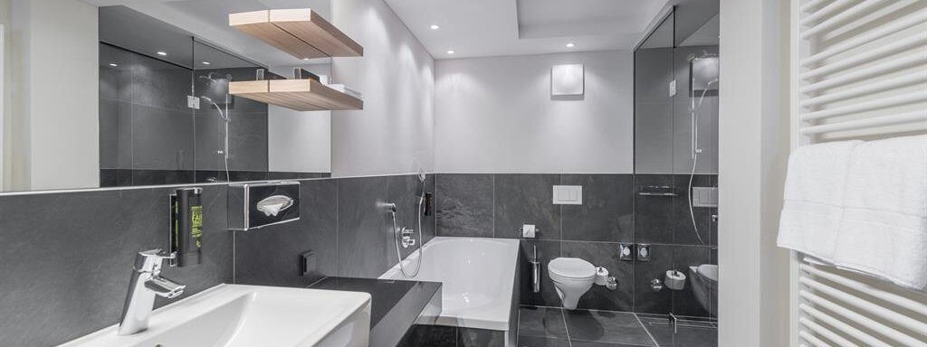 A modern bathroom with elegant black tiles and a large bathtub. Bright lighting and reflective surfaces create a pleasant atmosphere. - AlpenParks The Secret Sölden - Sölden