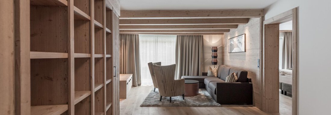 A bright and modern living room with wooden shelves and a large window. The furnishings are cozy and inviting with an armchair and a sofa. - AlpenParks The Secret Sölden - Sölden