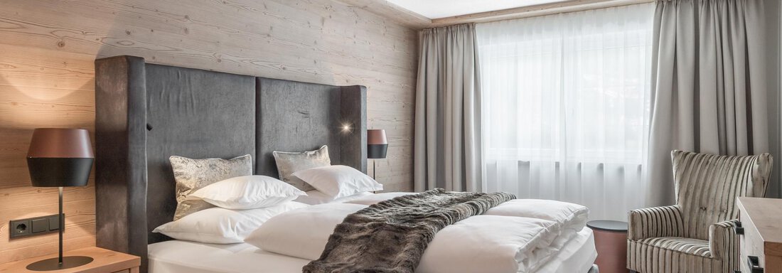 A modern hotel room with a large double bed and a comfortable seating area. Large windows provide plenty of natural light. - AlpenParks The Secret Sölden - Sölden