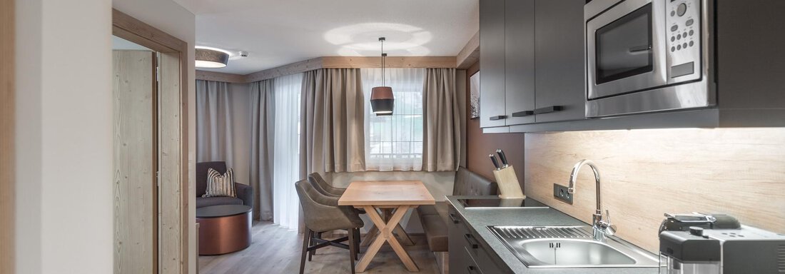 A modern kitchen with a dining table and elegant furniture. The space is bright and welcoming with wood and gray tones. - AlpenParks The Secret Sölden - Sölden