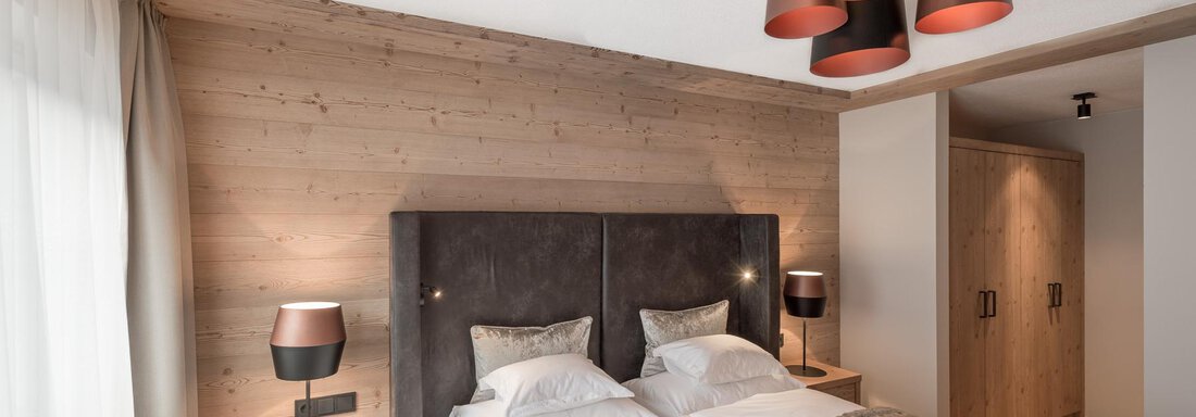 A stylish bedroom with a double bed and wooden paneling. Various light sources add a modern touch to the room. - AlpenParks The Secret Sölden - Sölden