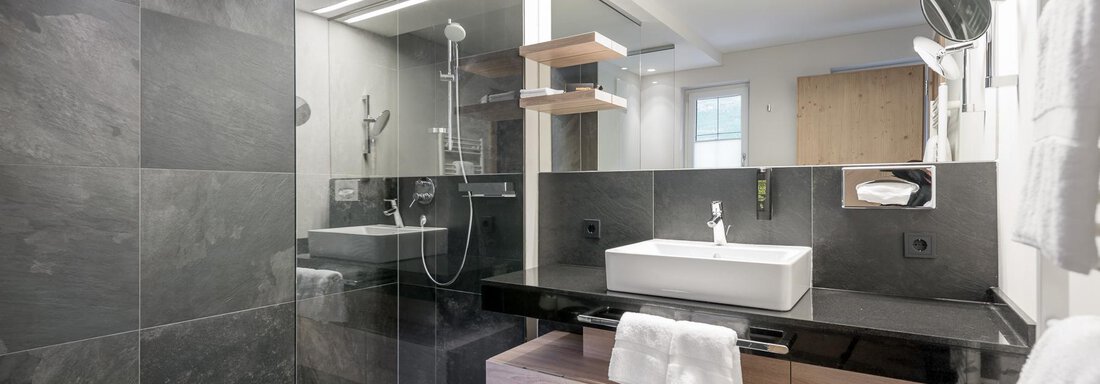 A modern bathroom with black tiles and an elegant shower. The wooden vanity and the large mirrors create a stylish atmosphere. - AlpenParks The Secret Sölden - Sölden
