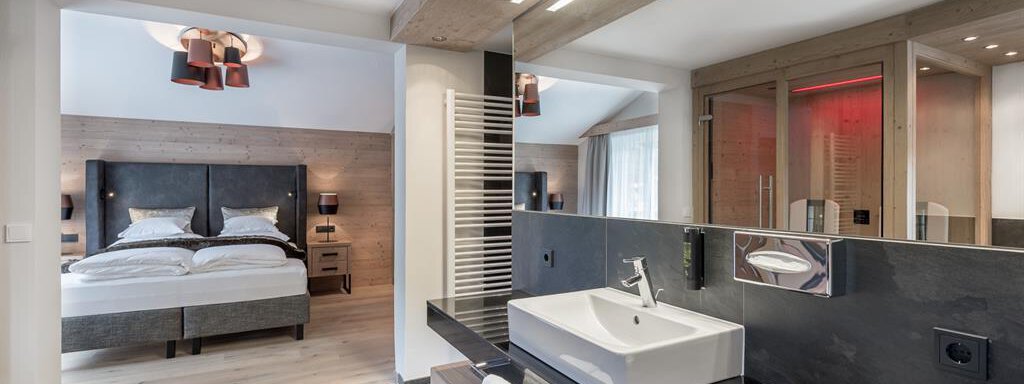 A modern bathroom with an elegant sink and mirror. In the background, you can see a cozy bedroom with a large bed. - AlpenParks The Secret Sölden - Sölden