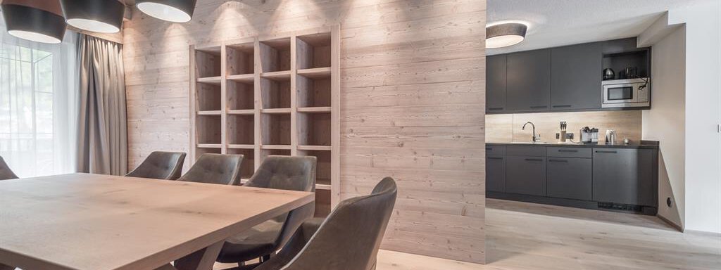A modern dining area with a large wooden table and comfortable chairs. In the background, a stylish kitchen is visible. - AlpenParks The Secret Sölden - Sölden