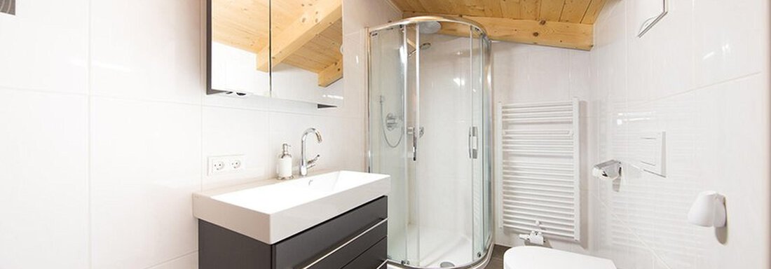 A modern bathroom with a shower, a sink, and a wooden ceiling. The walls are brightly tiled and the floor is laid with dark tiles. - Alpensweet - Sölden