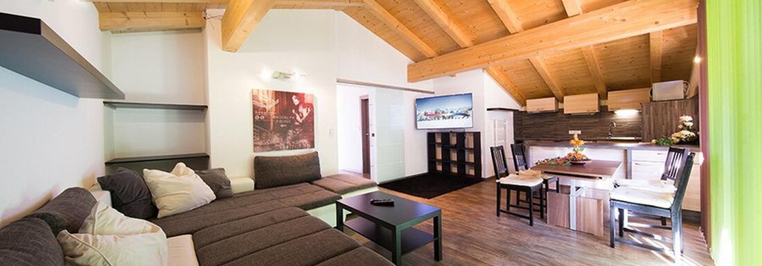 A modern living room with wooden ceilings and large windows. There is a cozy sofa, a table, and chairs for the dining areas. - Alpensweet - Sölden