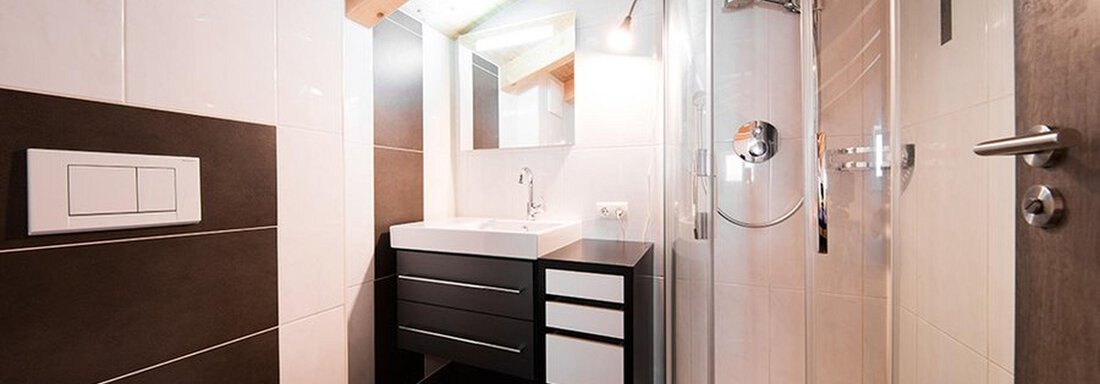 A modern bathroom with a shower, vanity, and wooden ceiling. The walls are light and the furnishings are functionally designed. - Alpensweet - Sölden