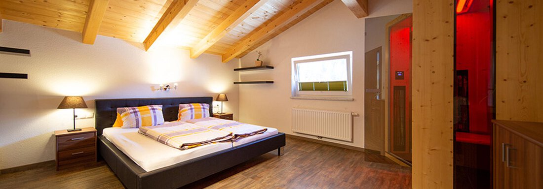 A modern bedroom with a wooden ceiling and stylish furniture. The room has a large bed and a sauna in the corner. - Alpensweet - Sölden