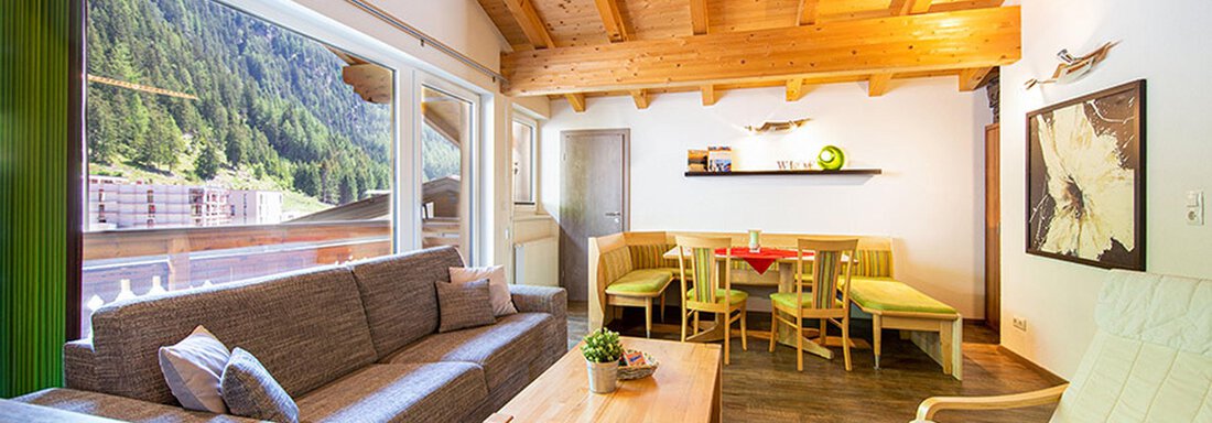 A cozy living space with a wooden ceiling and large windows. The room is furnished with a sofa, a dining table, and modern decor. - Alpensweet - Sölden