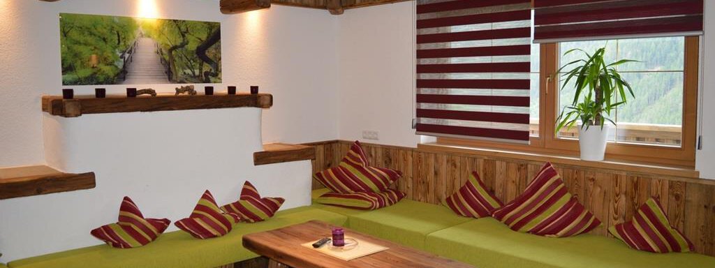 A cozy room with wooden paneling and a green bench. A picture hangs on the wall, and plants give the room a fresh touch. - Am Trogwohl - Sölden