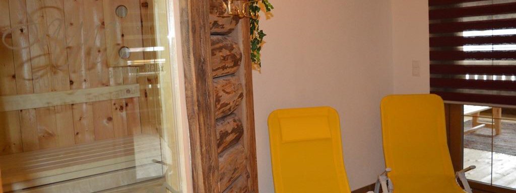 A cozy wellness area with a sauna and two yellow lounge chairs. The room is paneled with wood and offers a relaxing atmosphere. - Am Trogwohl - Sölden