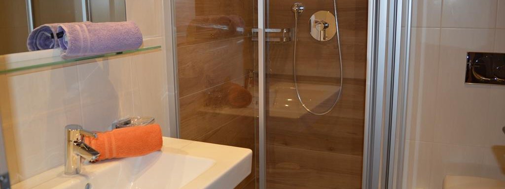 A modern bathroom with a shower and a sink. There are colored towels on the sink and a bright, elegant design. - Am Trogwohl - Sölden