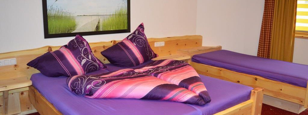 Dreibettzimmer A cozy bedroom with a wooden ceiling and two beds. The bed linens are purple with colorful pillows, and a picture hangs on the wall. - Am Trogwohl - Sölden