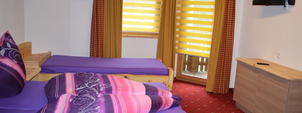 A cozy bedroom with two beds and colorful cushions. Large windows with yellow blinds provide plenty of daylight. - Am Trogwohl - Sölden