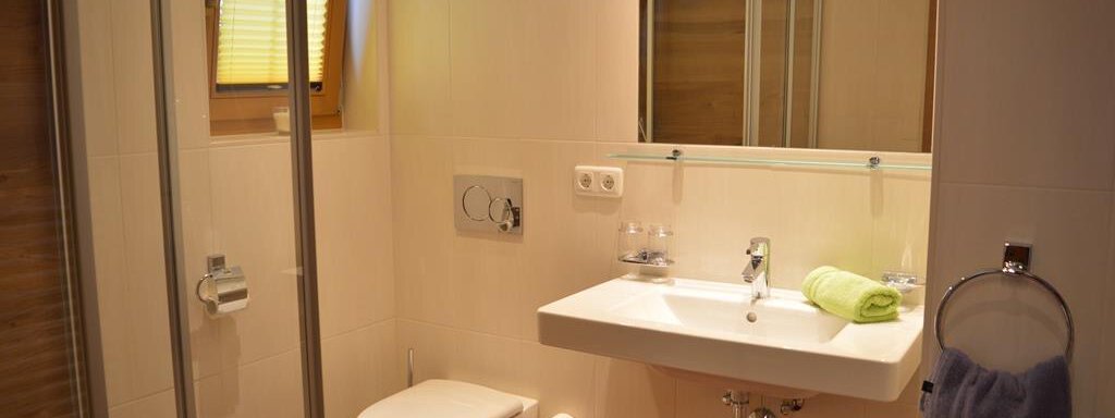 A modern bathroom with a shower and a sink. There are bright walls and large windows with yellow blinds. - Am Trogwohl - Sölden