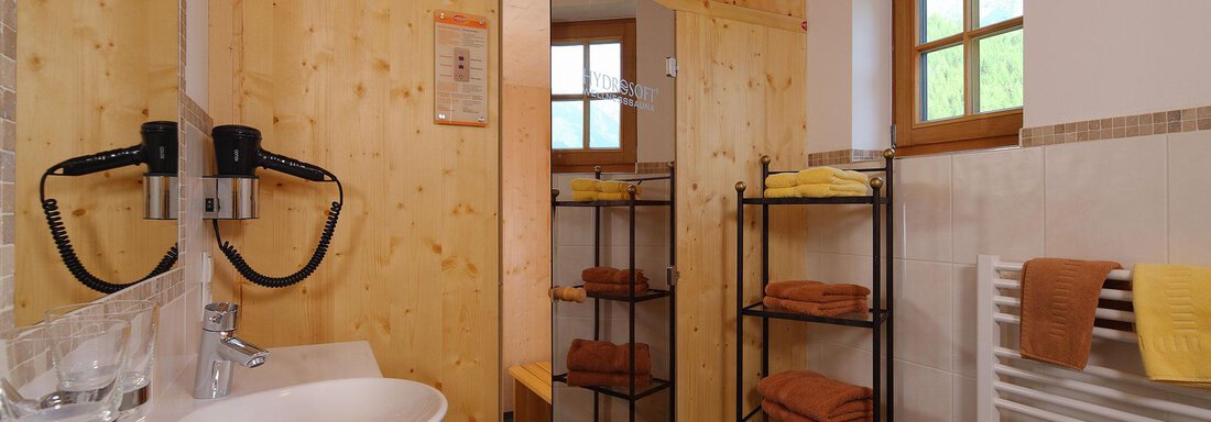 A modern bathroom with wood paneling and large windows. On a shelf, colorful towels are neatly stacked. - Andis Almdorf - Sölden