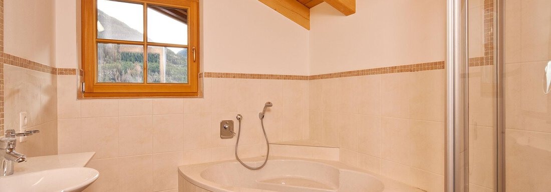 A modern bathroom with a round bathtub and a shower. Large windows provide plenty of daylight and a warm atmosphere. - Andis Almdorf - Sölden
