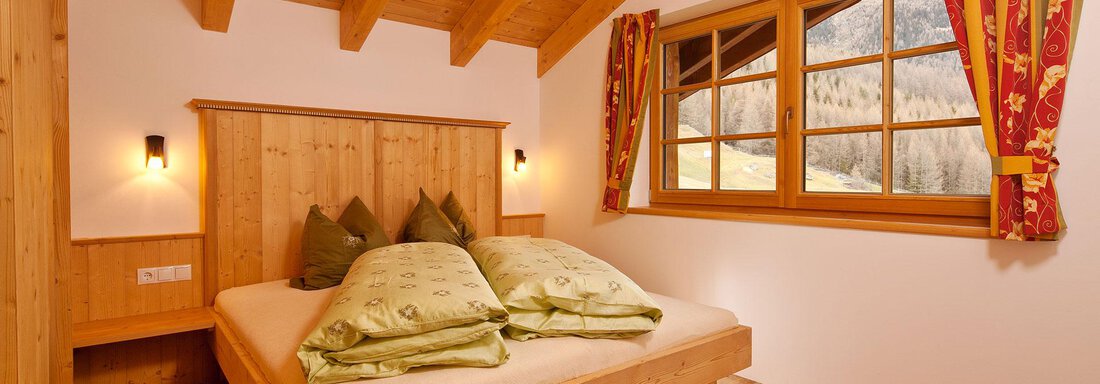 A cozy bedroom with a double bed and wooden decor. Large windows allow plenty of light in and offer a view of the landscape. - Andis Almdorf - Sölden