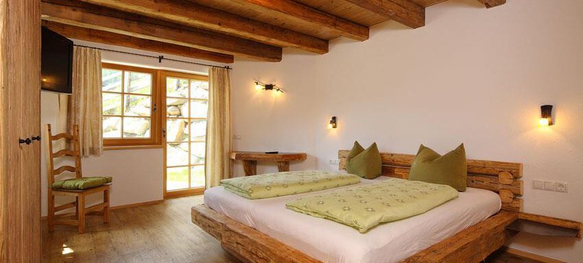 A cozy bedroom with a wooden bed and pillows in soft green tones. Large windows let in plenty of light, creating an inviting atmosphere. - Andis Almdorf - Sölden