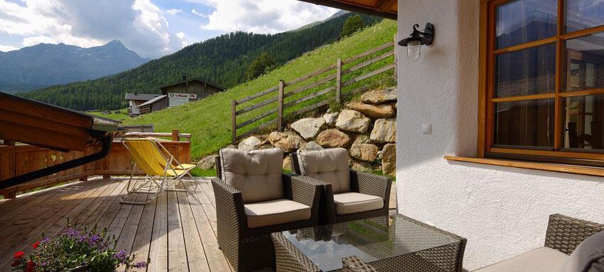 A beautiful outdoor area with cozy rattan furniture. The terrace offers a view of green hills and mountains. - Andis Almdorf - Sölden