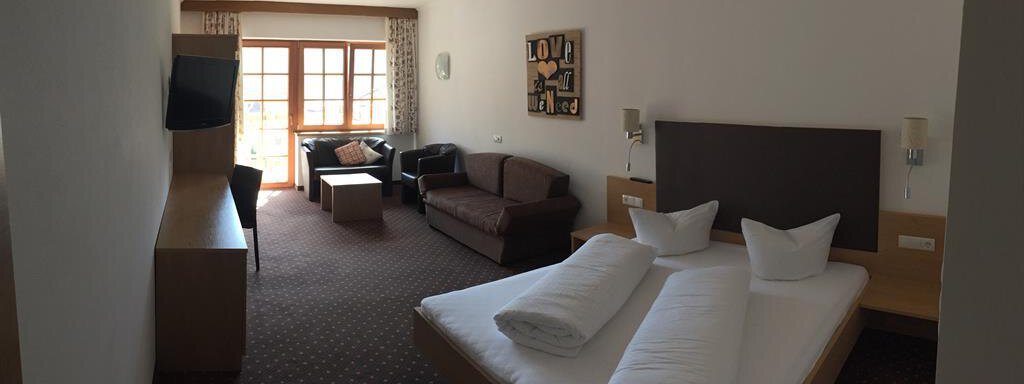 A cozy room with a double bed, a seating area, and a television. Large windows provide plenty of natural light and a pleasant view. - Andis Almdorf - Sölden