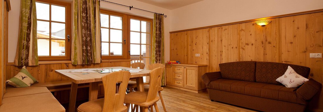 A cozy living space with wooden walls and a large table. Sofas and chairs create an inviting atmosphere. - Andis Almdorf - Sölden