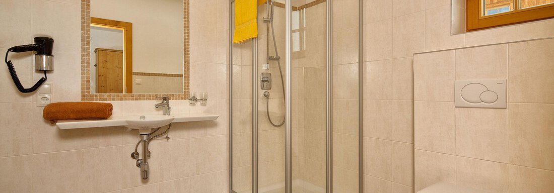 A modern bathroom with a shower, a sink, and a toilet. The walls are light tiled and there is a window with natural light. - Andis Almdorf - Sölden