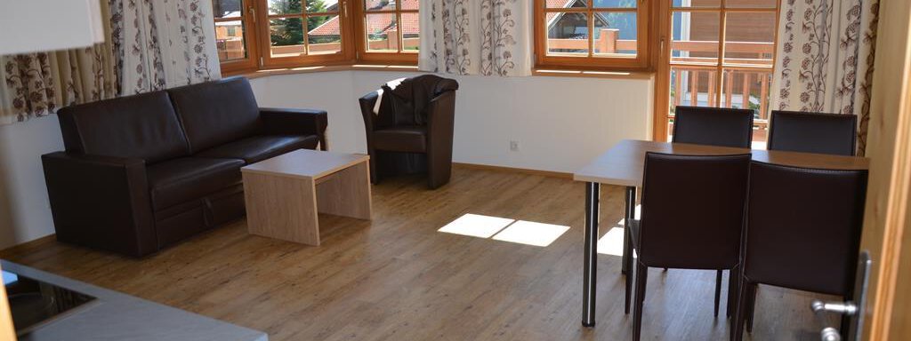 A bright living room with large windows and a cozy decor. There is a sofa, a table, and a dining table with chairs. - Andis Almdorf - Sölden