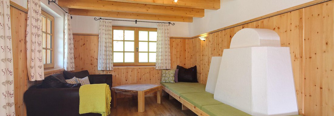 A cozy room with wooden walls and a wooden floor. There is a sofa, a table, and a small seating area with modern heating. - Andis Almdorf - Sölden