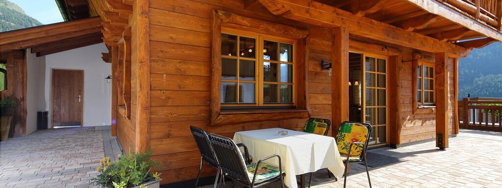 A cozy terrace with wooden cladding and garden furniture. In the background, the mountains are visible and the sky is clear. - Andis Almdorf - Sölden