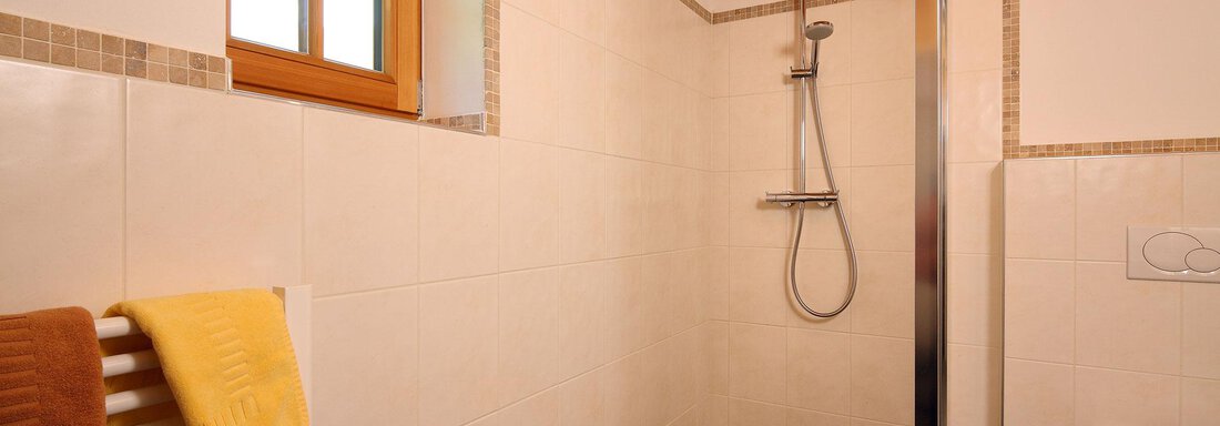 A modern bathroom with a shower and a large window. Towels in yellow and brown are laid out. - Andis Almdorf - Sölden
