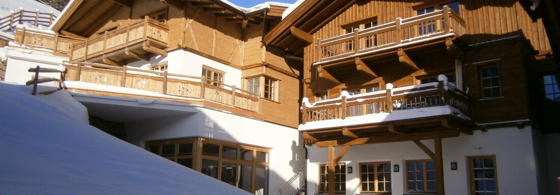 A cozy wooden building in the snow with balconies and a clear blue sky. The surroundings look wintery and inviting. - Andis Almdorf - Sölden