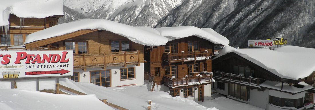 An idyllic ski restaurant surrounded by snow-covered mountains. The buildings are covered in snow, and the landscape radiates winter tranquility. - Andis Almdorf - Sölden
