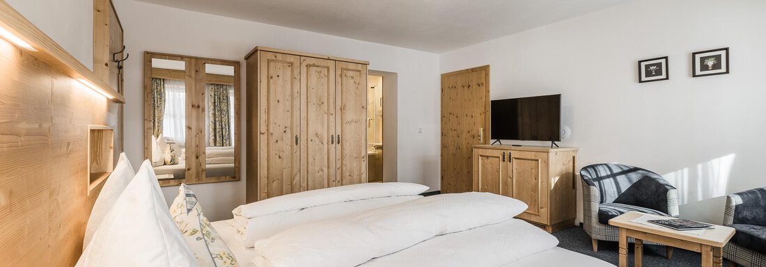 A cozy hotel room with two beds and modern wooden paneling. There is a television, a small table, and a wardrobe in the background. - Andre Arnold - Boutique Hotel - Sölden