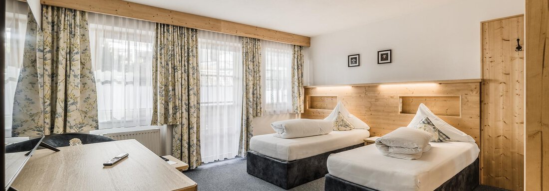 A bright room with two single beds and a large window. The decor is cozy and modern, with wooden details and a friendly atmosphere. - Andre Arnold - Boutique Hotel - Sölden