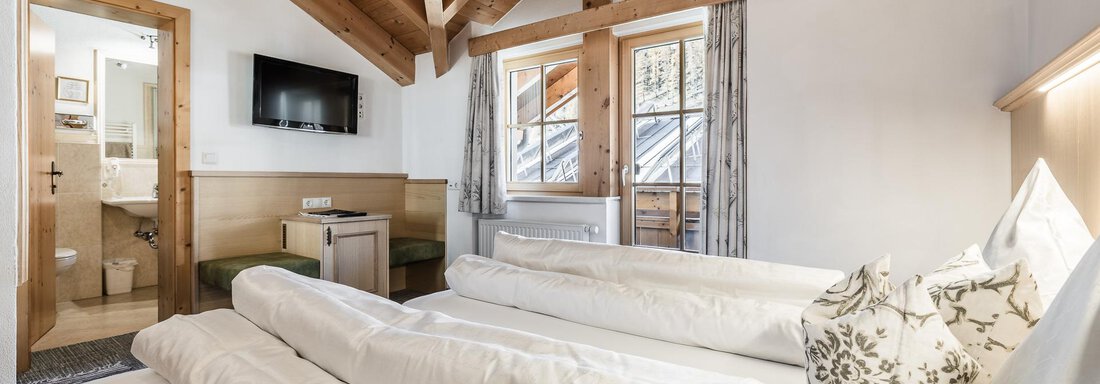A cozy room with a wooden ceiling and large windows. It features a double bed and a television. - Andre Arnold - Boutique Hotel - Sölden