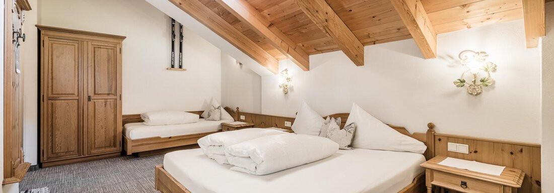 A cozy bedroom with a wooden ceiling and two beds. The room has a warm, inviting atmosphere and plenty of natural light. - Andre Arnold - Boutique Hotel - Sölden