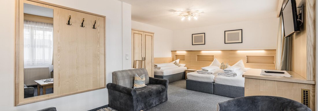 A modern hotel room with two beds, a seating area, and a large mirror. The room is bright and comfortably furnished. - Andre Arnold - Boutique Hotel - Sölden