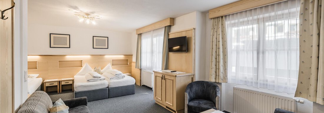 A cozy room with two beds, a seating area, and a table. Large windows provide plenty of daylight. - Andre Arnold - Boutique Hotel - Sölden