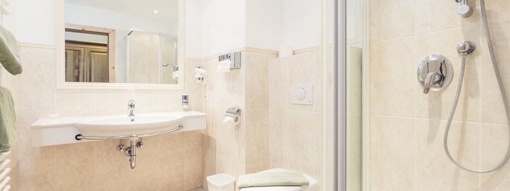 A modern bathroom with a shower, a sink, and a toilet. The walls are brightly tiled, and there is a large mirror. - Andre Arnold - Boutique Hotel - Sölden