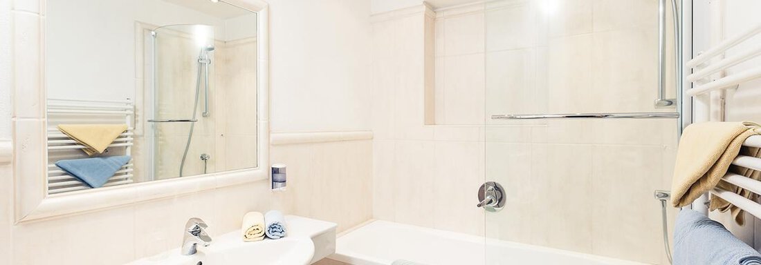 A modern bathroom with a bathtub and a shower. The walls are bright and there are towels in gentle colors. - Andre Arnold - Boutique Hotel - Sölden