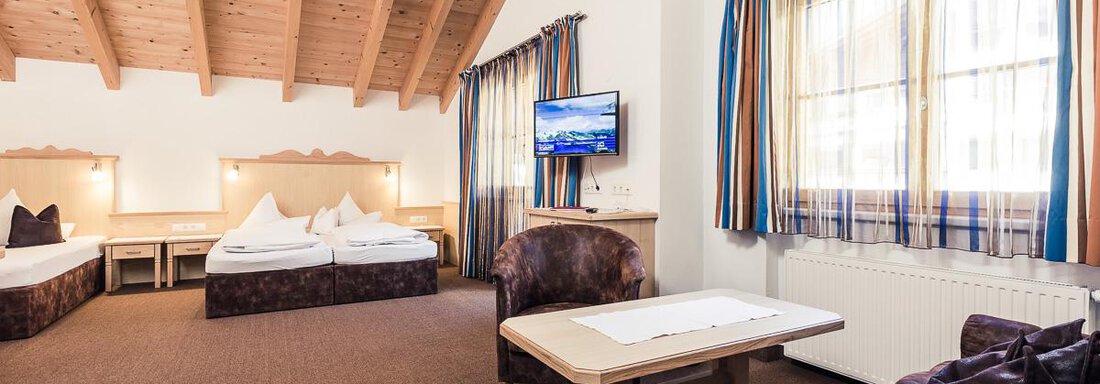 A spacious room with two beds and a cozy sofa.  
Large windows let in plenty of light and create an inviting atmosphere. - Andre Arnold - Boutique Hotel - Sölden