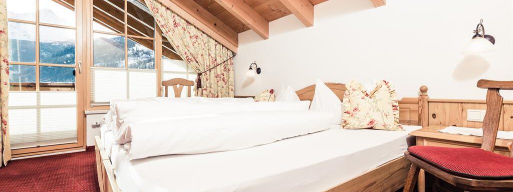 A cozy bedroom with a double bed and wooden furniture. Large windows offer a beautiful view of the mountains. - Andre Arnold - Boutique Hotel - Sölden