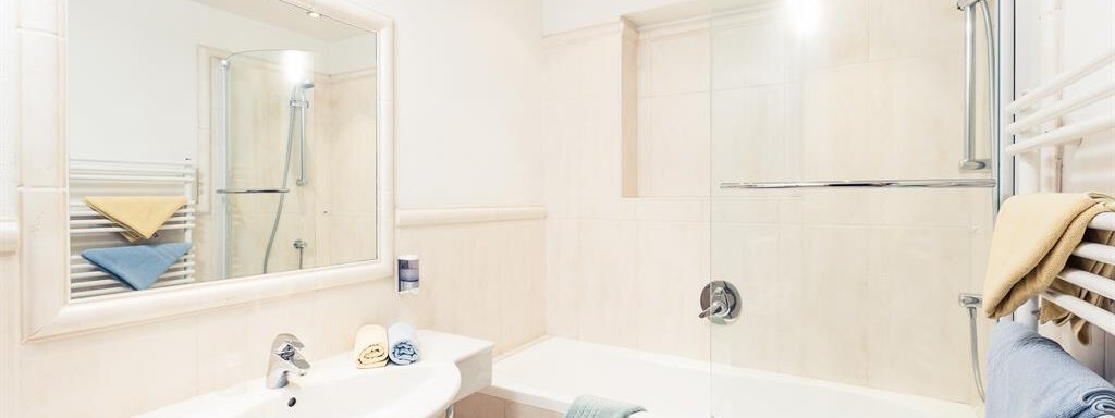 A modern bathroom with a bathtub and a shower. Bright tiles and a large mirrored wall create a spacious atmosphere. - Andre Arnold - Boutique Hotel - Sölden