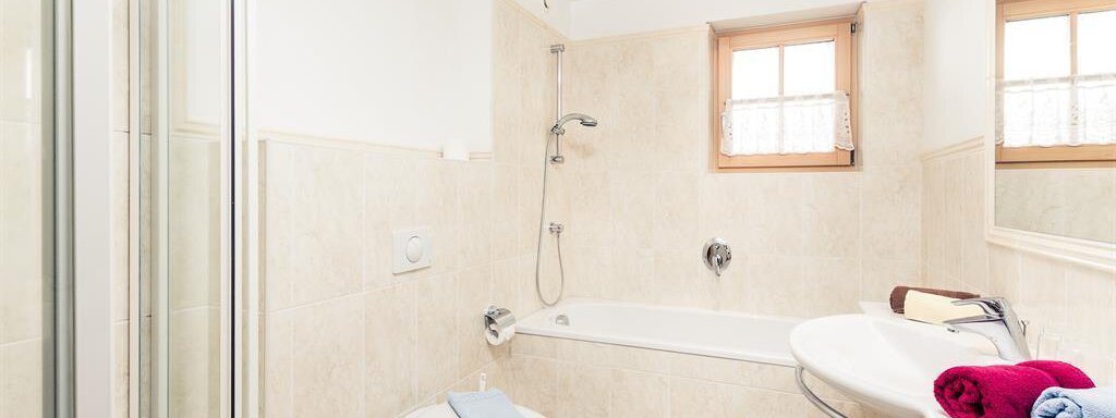 A modern bathroom with a shower and a bathtub. There are towels in various colors and a window that lets daylight shine in. - Andre Arnold - Boutique Hotel - Sölden